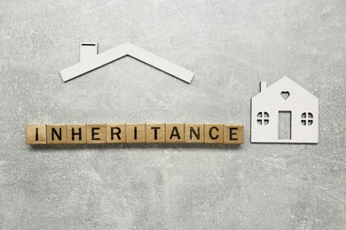 Word Inheritance made with wooden cubes and house model on grey background, flat lay
