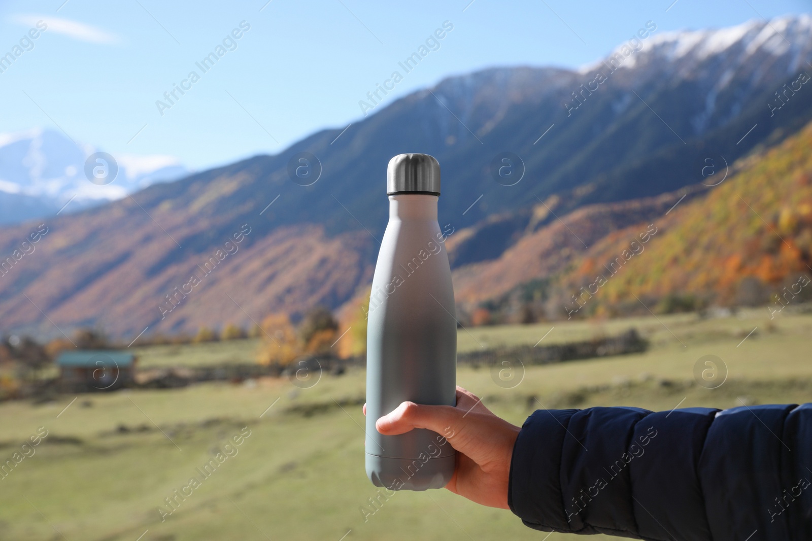 Photo of Boy holding thermo bottle with drink in mountains on sunny day, closeup