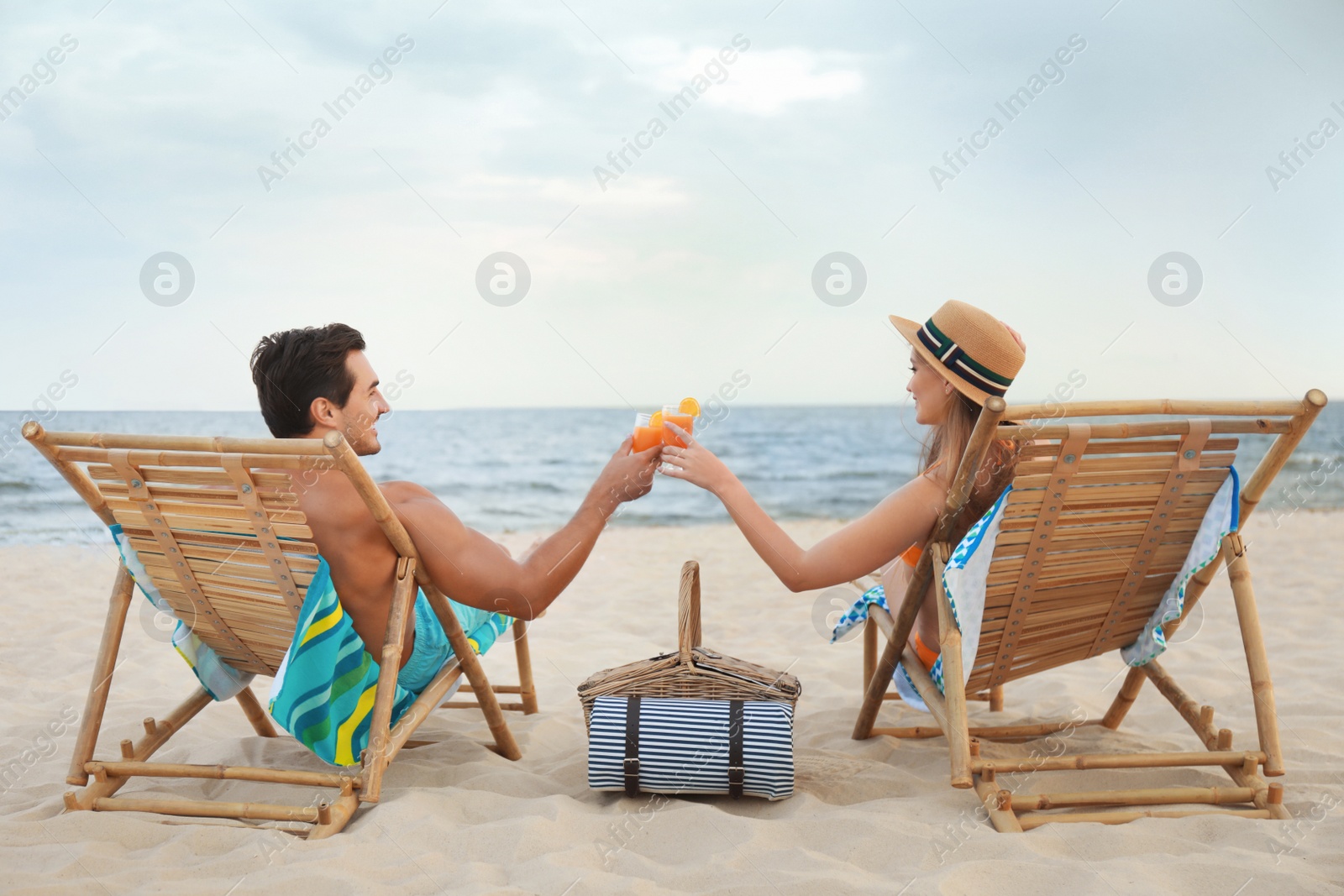 Photo of Happy young couple with cocktails sitting on deck chairs at sea beach