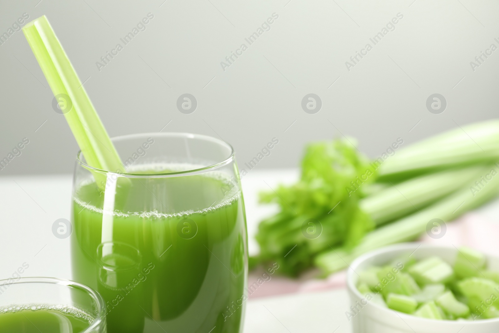 Photo of Glass of delicious celery juice and vegetables on white table, closeup. Space for text