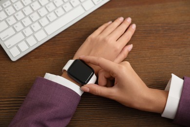Image of Woman using stylish smart watch at wooden table, closeup