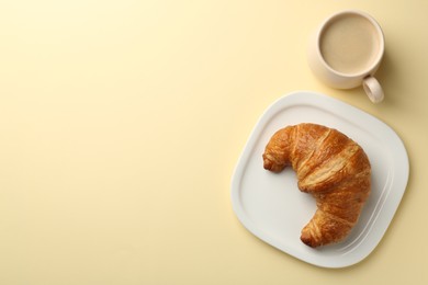 Photo of Delicious fresh croissant and cup of coffee on beige table, flat lay. Space for text