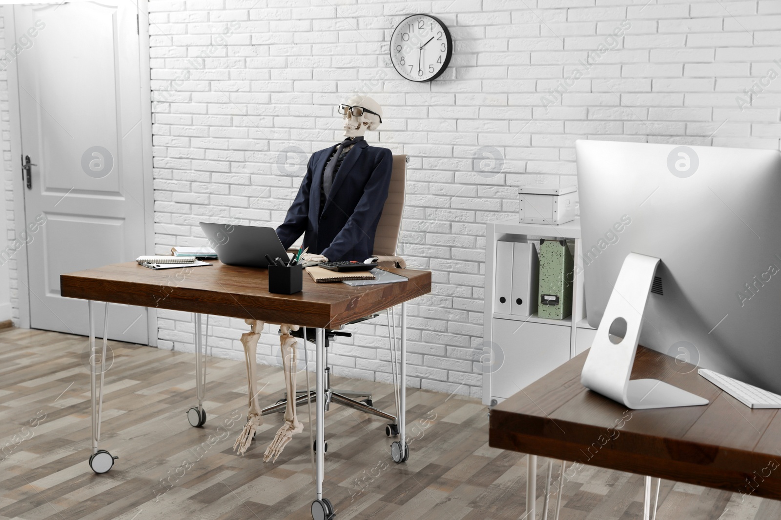 Photo of Human skeleton in suit using laptop at table in office