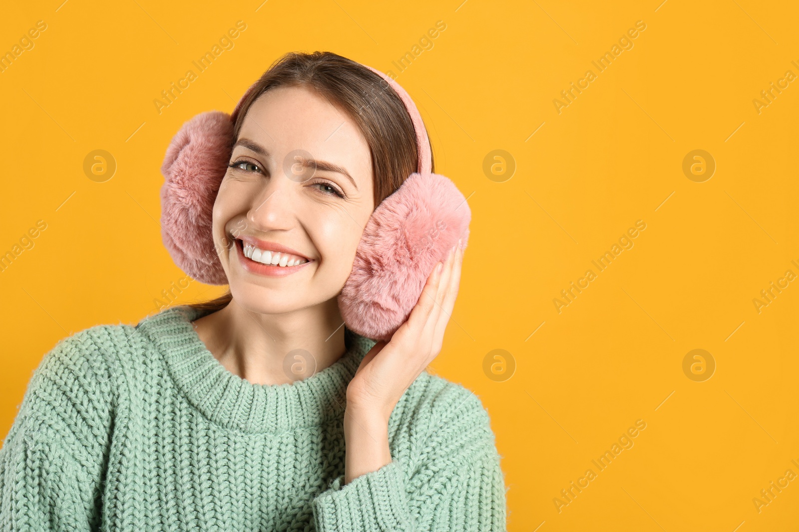 Photo of Happy woman wearing warm earmuffs on yellow background, space for text