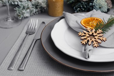 Photo of Festive place setting with beautiful dishware, fabric napkin and dried orange slice for Christmas dinner on grey table, closeup