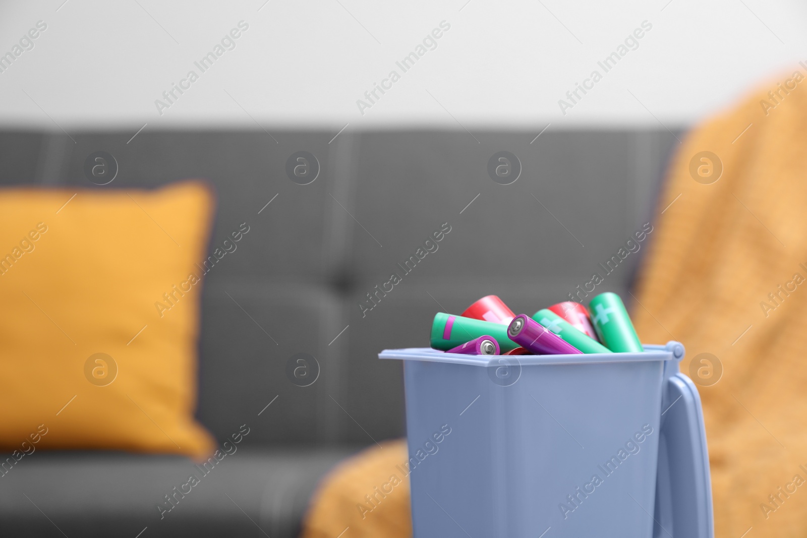 Photo of Mini recycling bin with different types of batteries indoors, closeup. Space for text