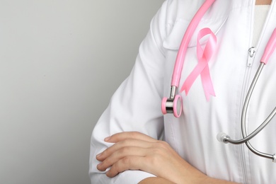 Photo of Doctor with pink ribbon and stethoscope on grey background, space for text. Breast cancer awareness