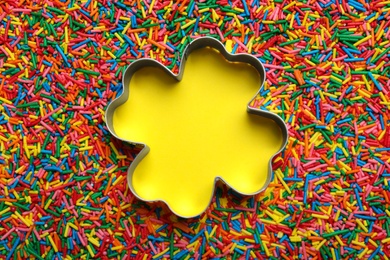 Photo of Clover shaped cookie cutter and sprinkles on yellow background, flat lay with space for text. Confectionery decor