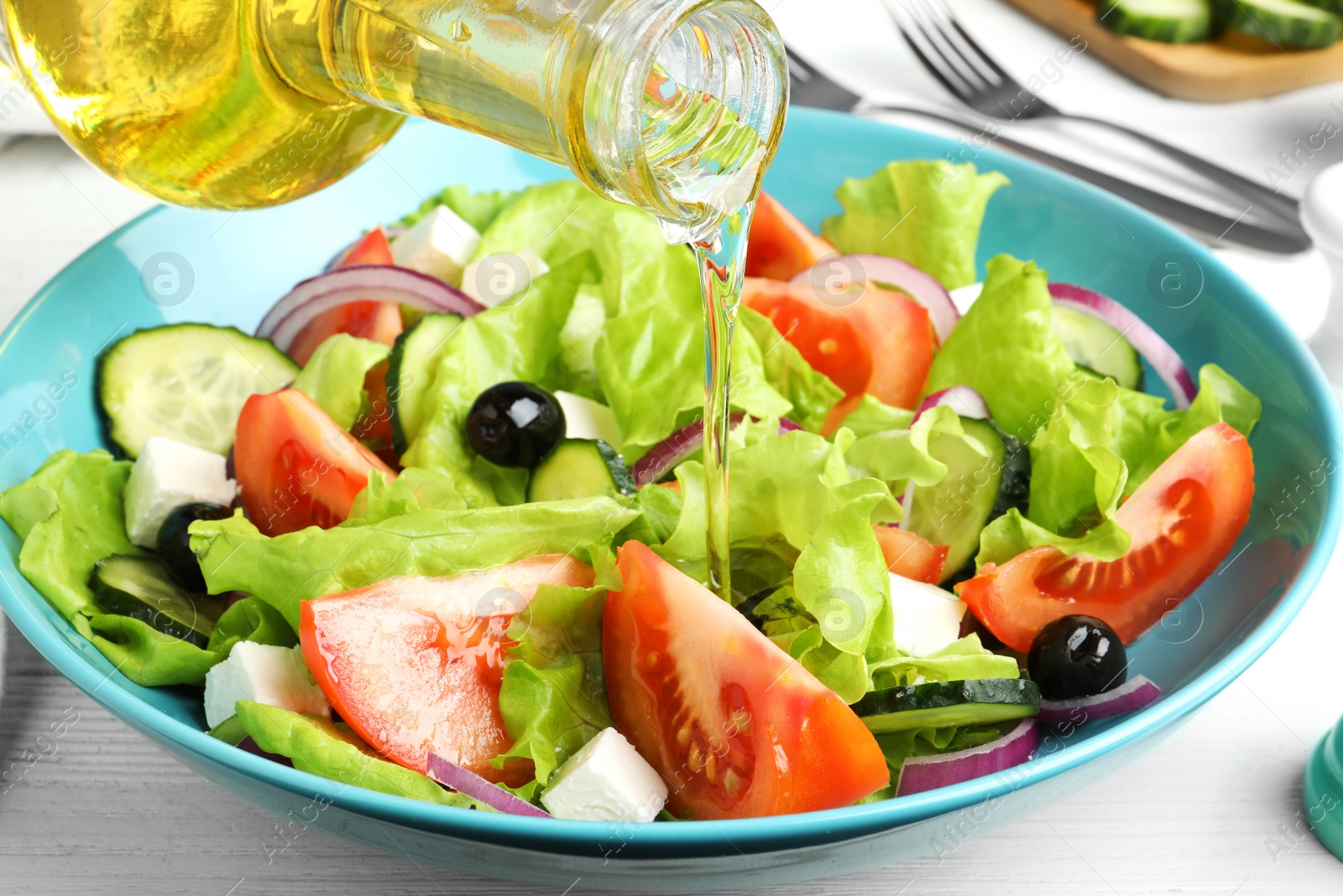 Photo of Adding cooking oil to delicious salad on table, closeup