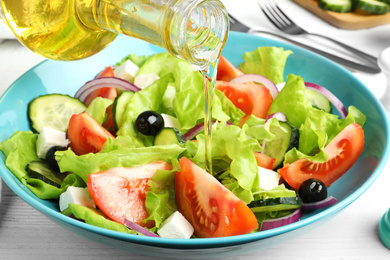 Adding cooking oil to delicious salad on table, closeup