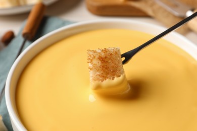 Photo of Dipping piece of bread into tasty cheese fondue, closeup