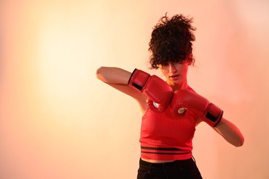 Photo of Beautiful young woman with boxing gloves on color background in neon lights. Space for text