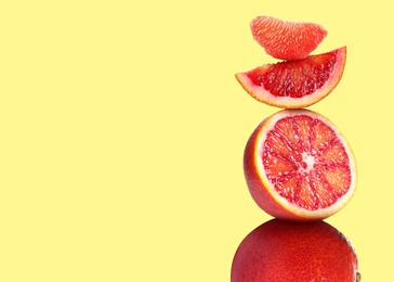 Stacked cut and whole red oranges on pale light yellow background, space for text