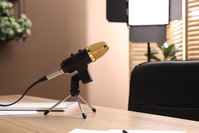 Tripod with modern microphone on wooden table in room. Blogger's workplace