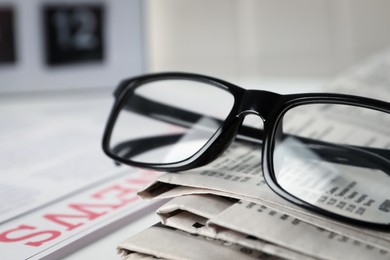 Glasses on stack of newspapers, closeup view