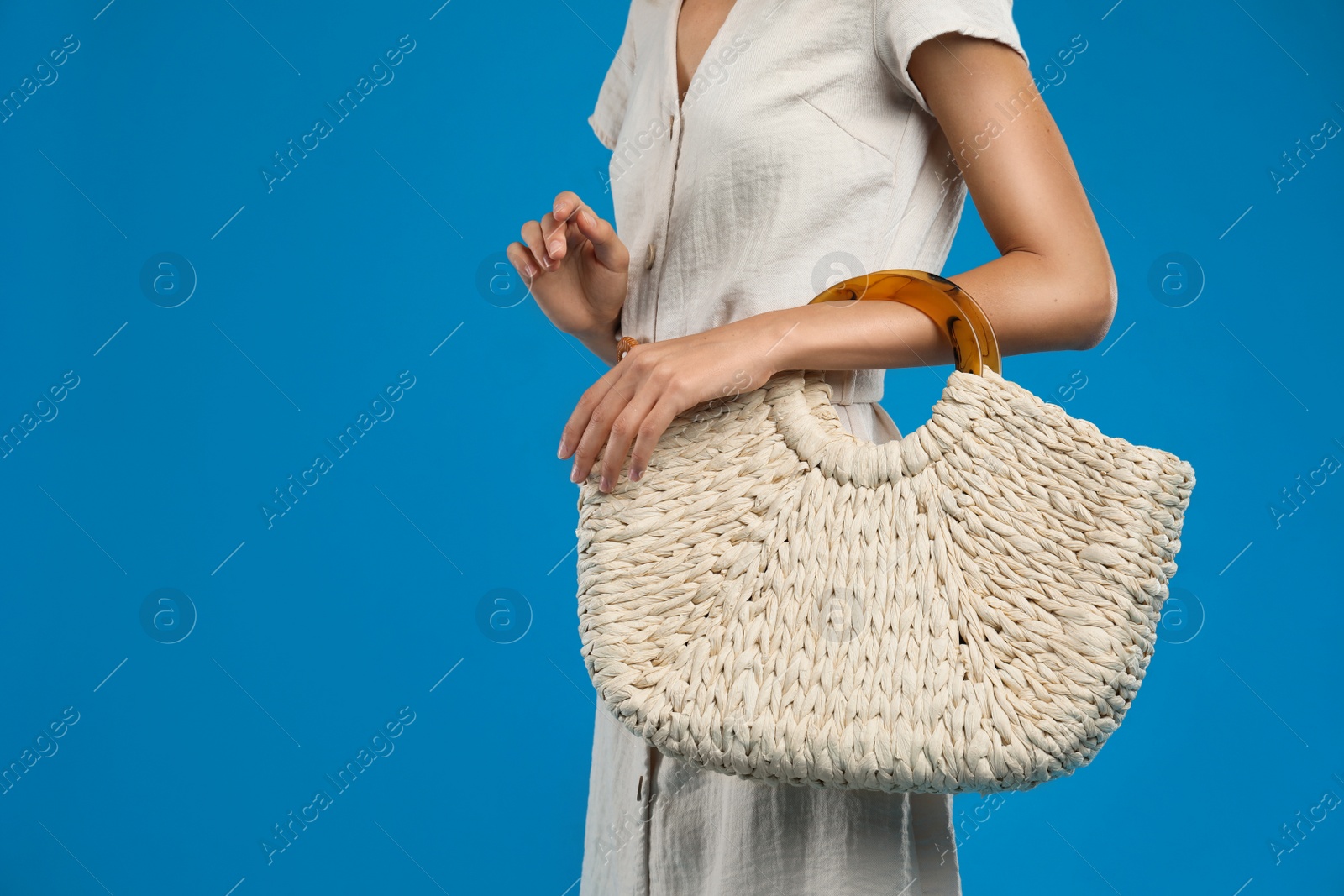 Photo of Young woman with stylish straw bag on blue background, closeup. Space for text