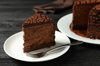 Photo of Piece of delicious chocolate truffle cake and fork on black wooden table, closeup