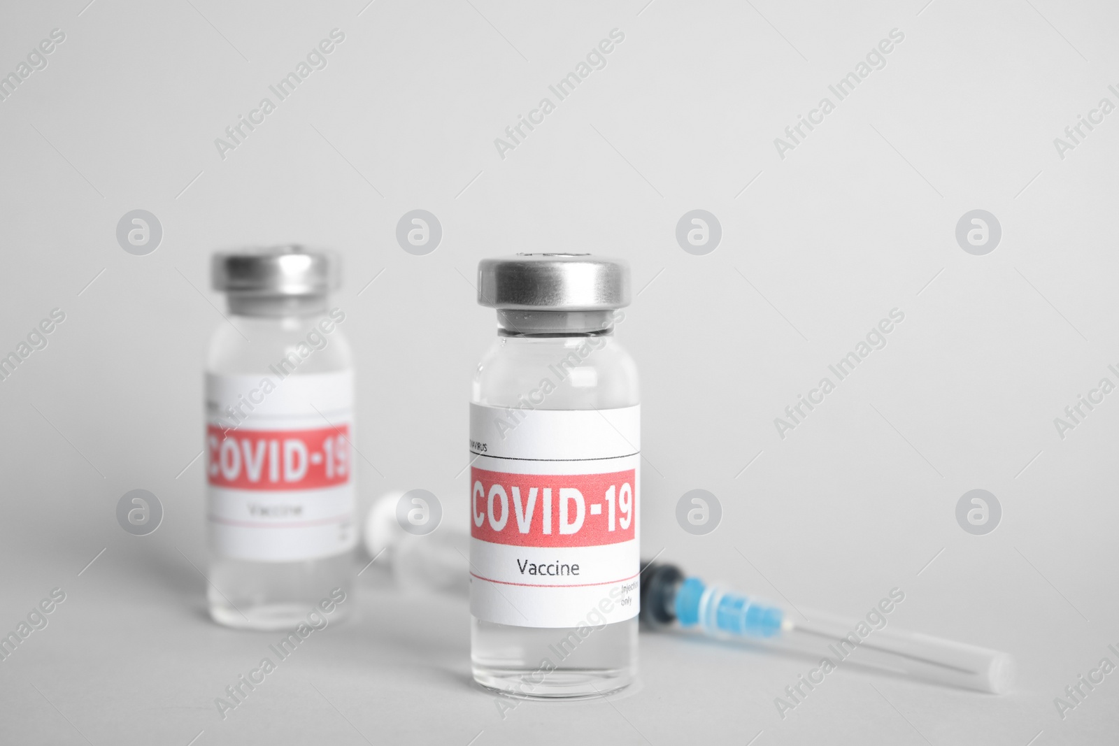 Photo of Vials with coronavirus vaccine and syringe on light background