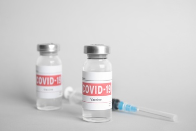 Vials with coronavirus vaccine and syringe on light background