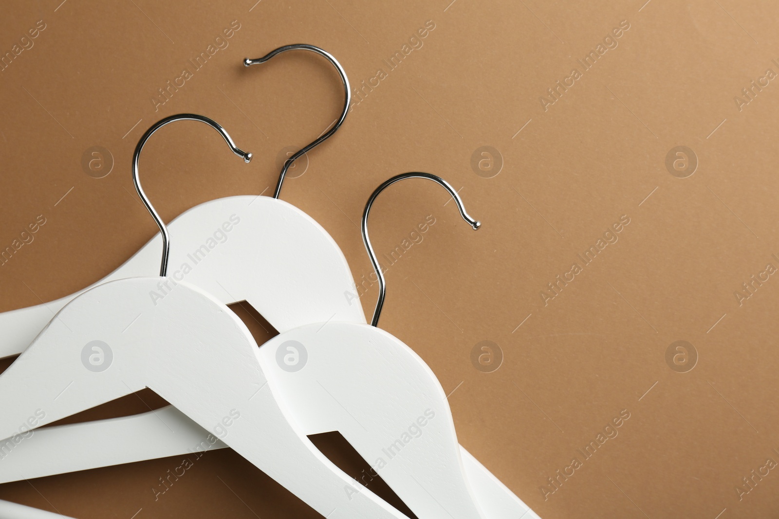 Photo of White hangers on brown background, top view. Space for text