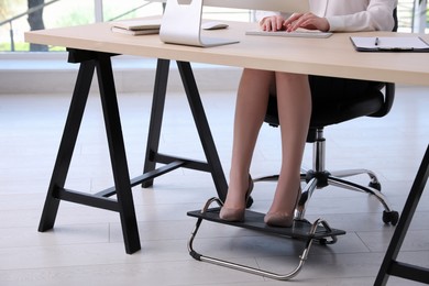 Photo of Woman using footrest while working on computer in office, closeup