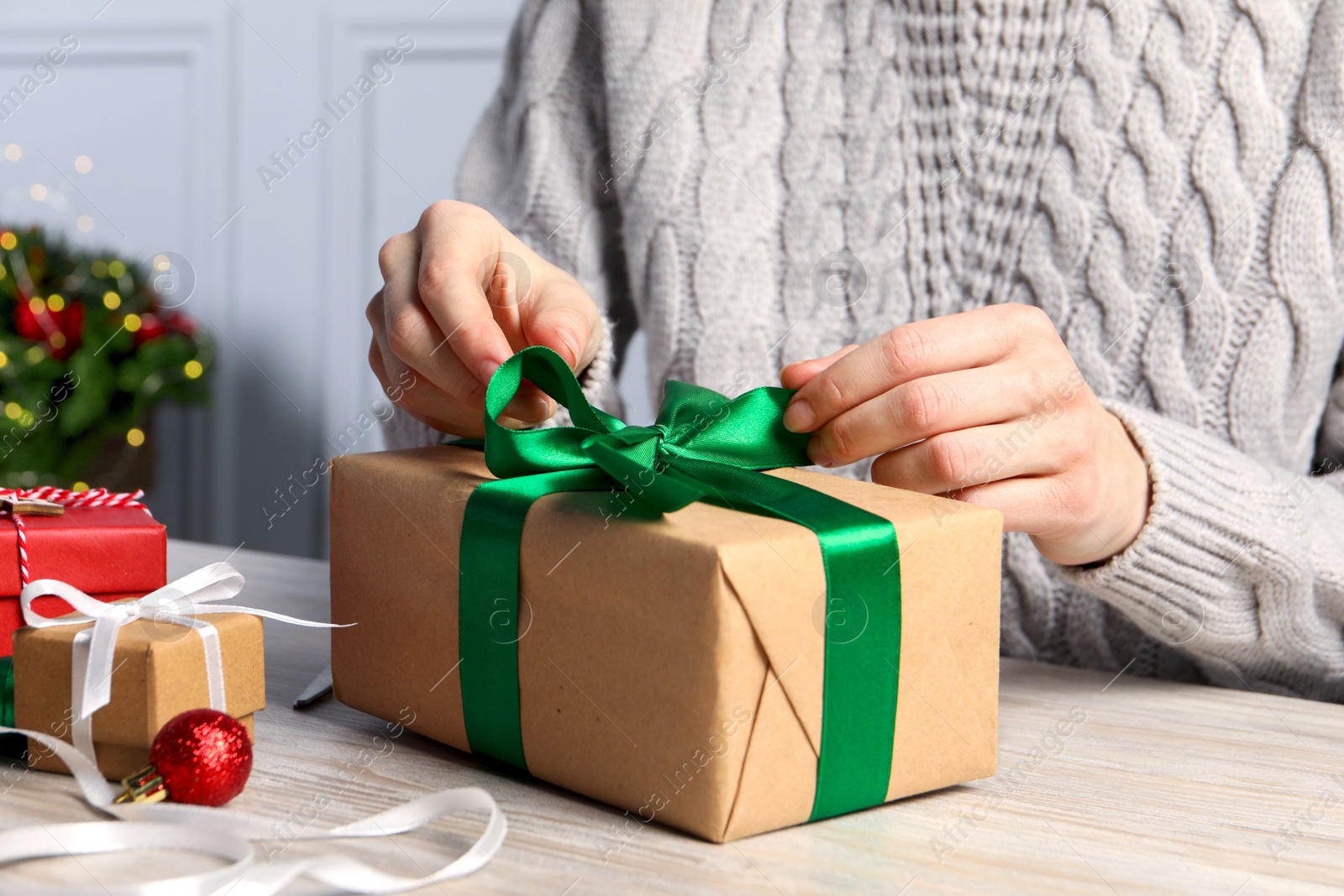 Photo of Woman decorating gift box at white wooden table, closeup. Christmas present