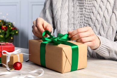 Woman decorating gift box at white wooden table, closeup. Christmas present