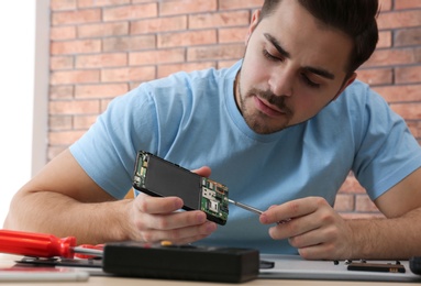 Photo of Technician repairing broken smartphone at table in workshop