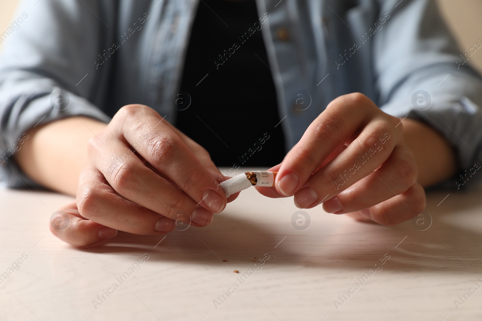 Photo of Stop smoking. Woman holding broken cigarette at table, closeup