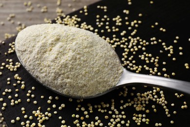 Photo of Spoon with quinoa flour and seeds on black wooden table, closeup