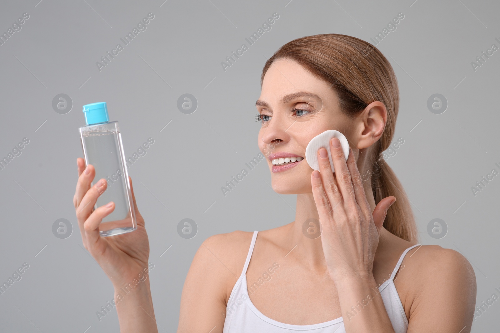 Photo of Beautiful woman removing makeup with cotton pad on gray background