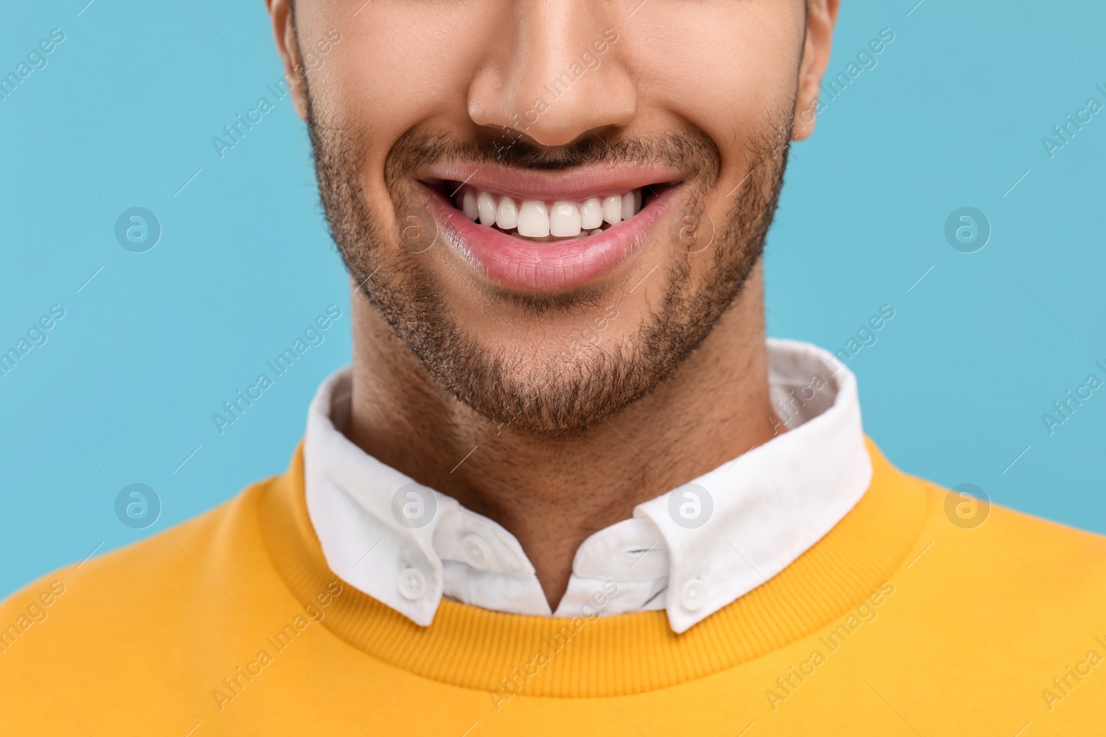 Photo of Smiling man with healthy clean teeth on light blue background, closeup