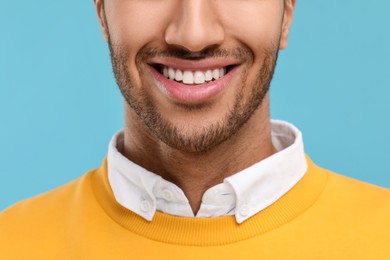 Smiling man with healthy clean teeth on light blue background, closeup