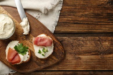 Photo of Delicious sandwiches with cream cheese and jamon on wooden table, flat lay. Space for text