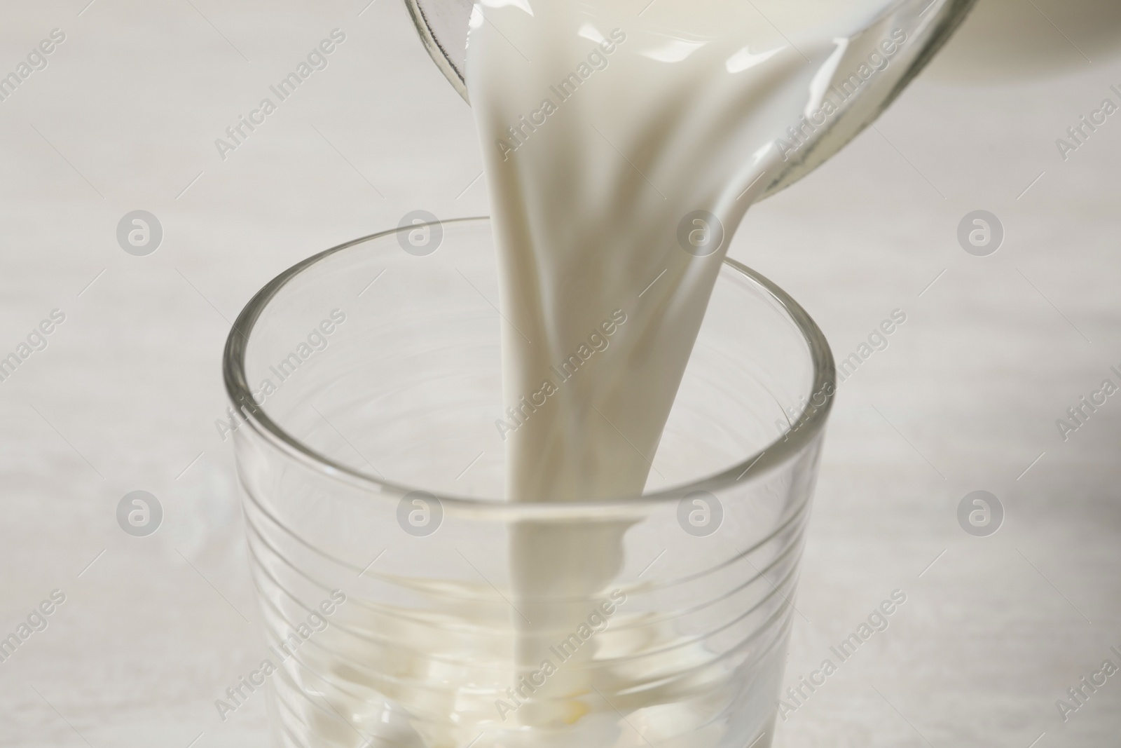 Photo of Pouring milk into glass on white table, closeup