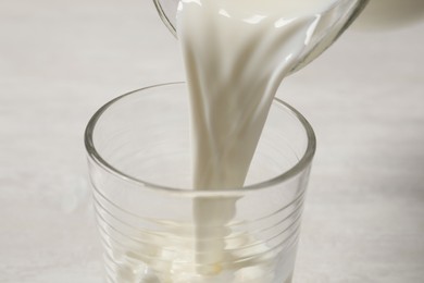 Photo of Pouring milk into glass on white table, closeup