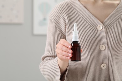 Woman holding nasal spray indoors, closeup. Space for text