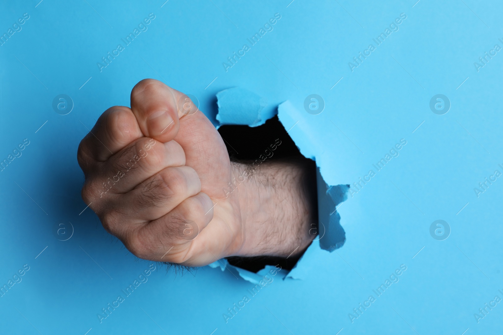 Photo of Man breaking through light blue paper with fist, closeup