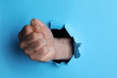 Man breaking through light blue paper with fist, closeup