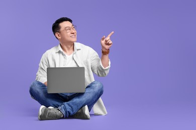 Photo of Happy man with laptop pointing at something on lilac background, space for text