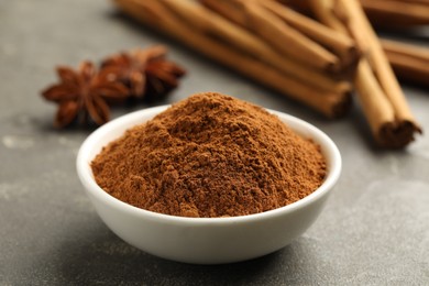 Photo of Bowl of cinnamon powder on grey table, closeup