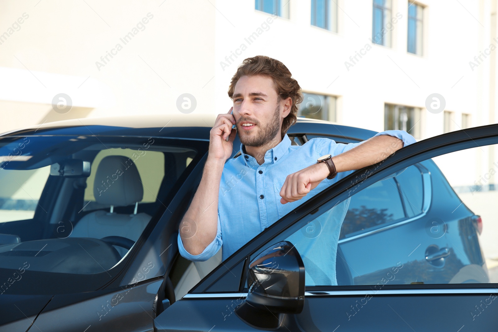 Photo of Young man talking on phone near modern car, outdoors