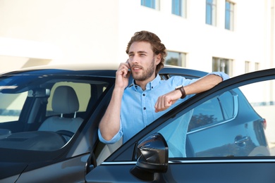 Young man talking on phone near modern car, outdoors