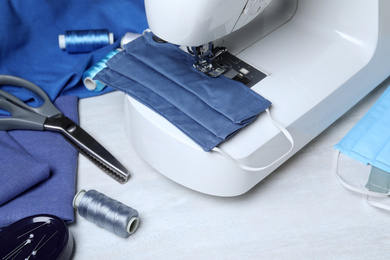 Photo of Sewing machine with homemade protective mask and craft accessories on white table