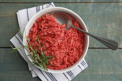 Photo of Fresh minced meat and spoon in bowl on light blue wooden table, top view