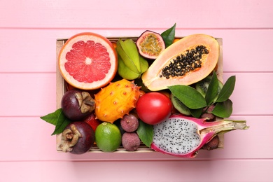 Different tropical fruits in box on pink wooden background, top view