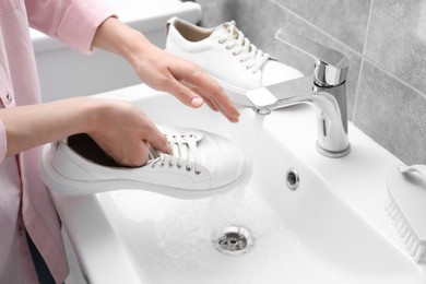 Woman washing stylish sneakers in sink, closeup