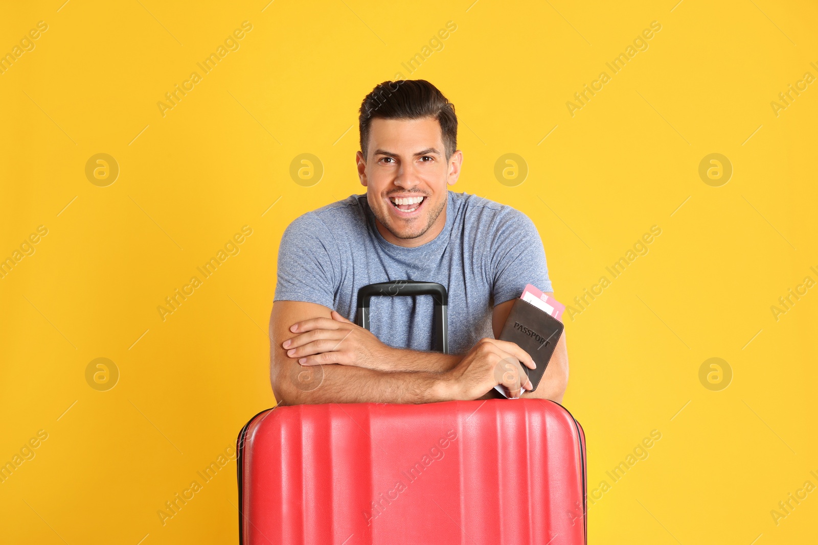 Photo of Handsome man with suitcase and ticket in passport for summer trip on yellow background. Vacation travel