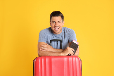 Photo of Handsome man with suitcase and ticket in passport for summer trip on yellow background. Vacation travel