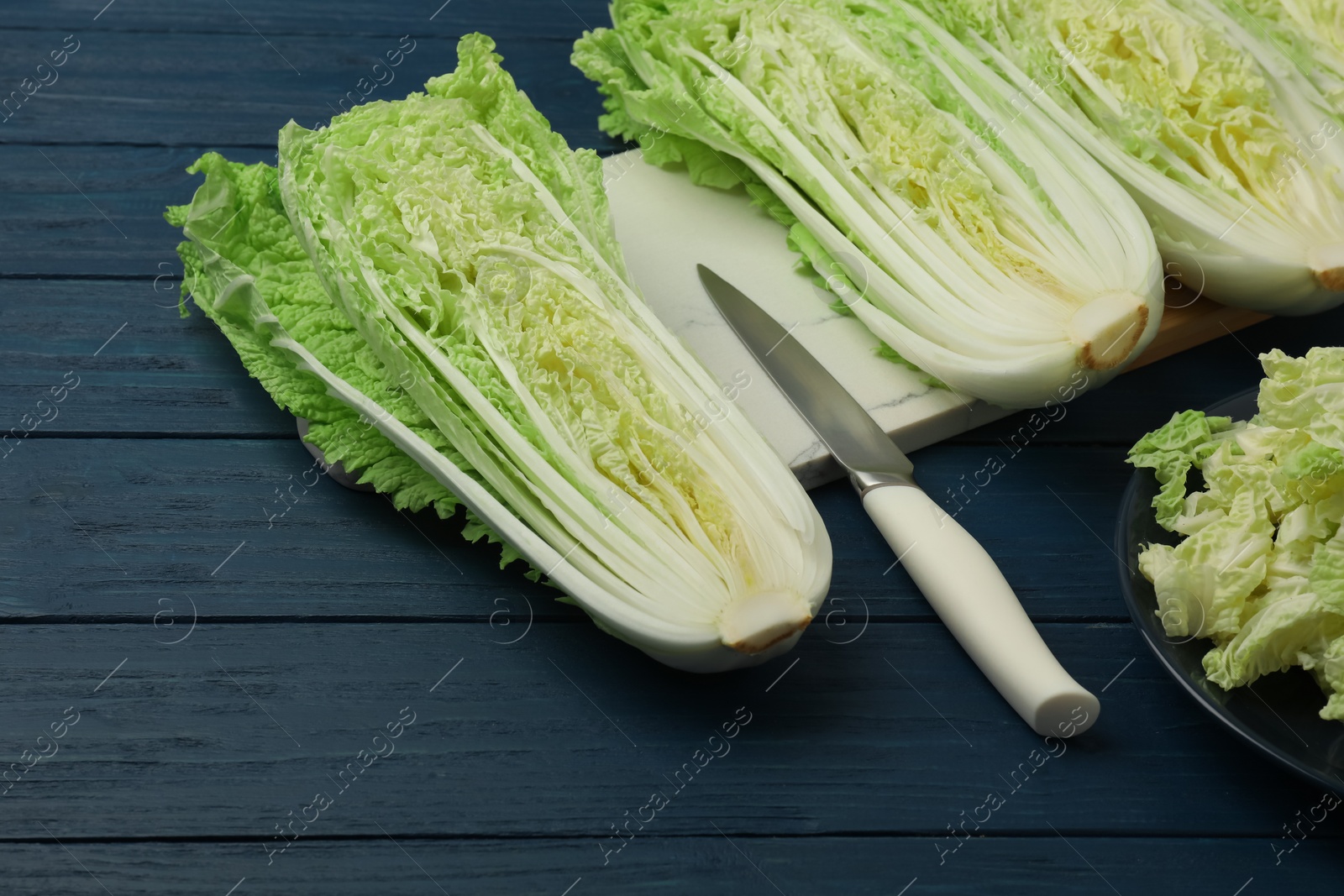 Photo of Cut fresh ripe Chinese cabbages on blue wooden table